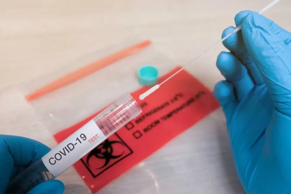 Gloved hands handling a sealed COVID-19 test specimen bag